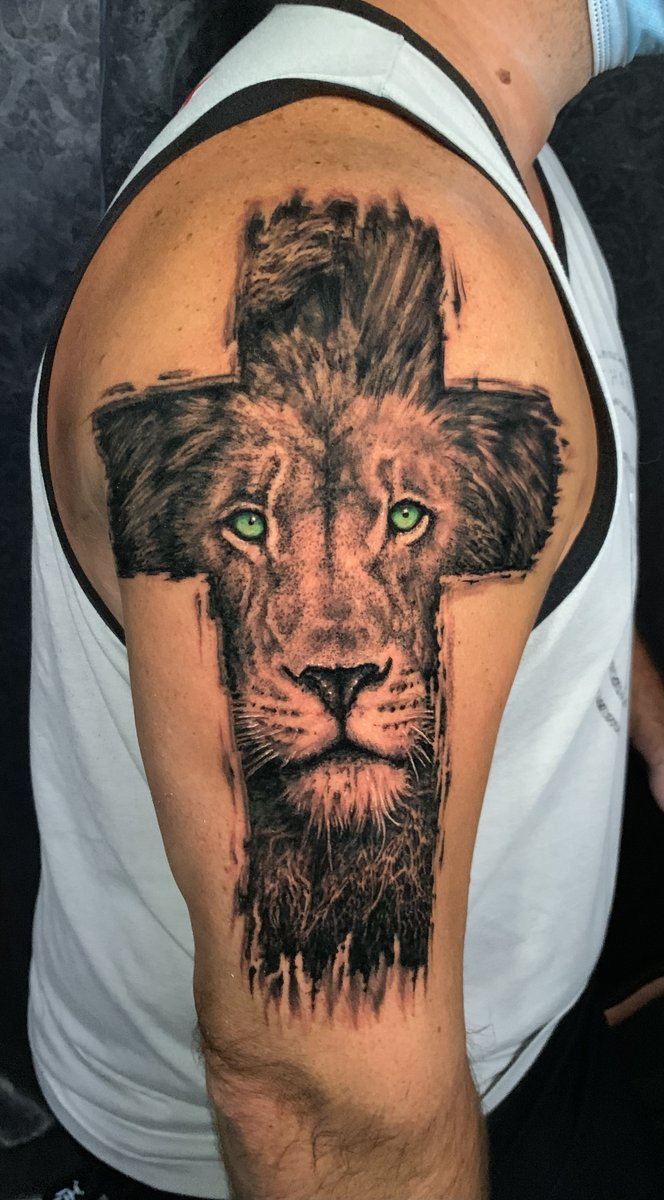 Black and gray lion face merged with Christian cross upper arm tattoo with vivid green eyes by Zack Ross, custom tattoo artist Kyle TX serving Austin and Dallas Texas